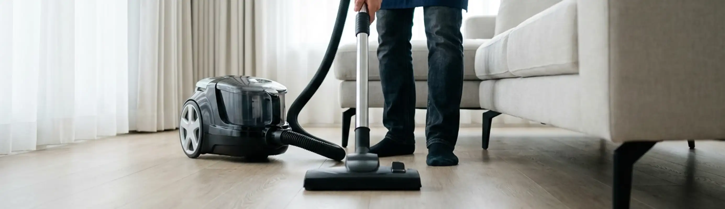 Professional house cleaner vacuuming a living room floor with a canister vacuum cleaner, Des Moines, IA.