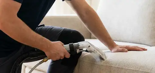 Professional upholstery cleaner deep-cleaning a fabric sofa with a handheld extraction tool, Des Moines, IA.