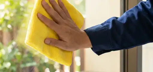 House cleaner wiping a glass window with a yellow microfiber cloth for streak-free cleaning, Des Moines, IA.